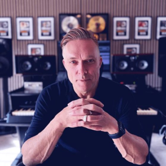 Candid studio photograph of ambient and trance artist Nicholas Gunn creating electronic music, surrounded by synthesizers used to produce his signature melodic house and chillout tracks.